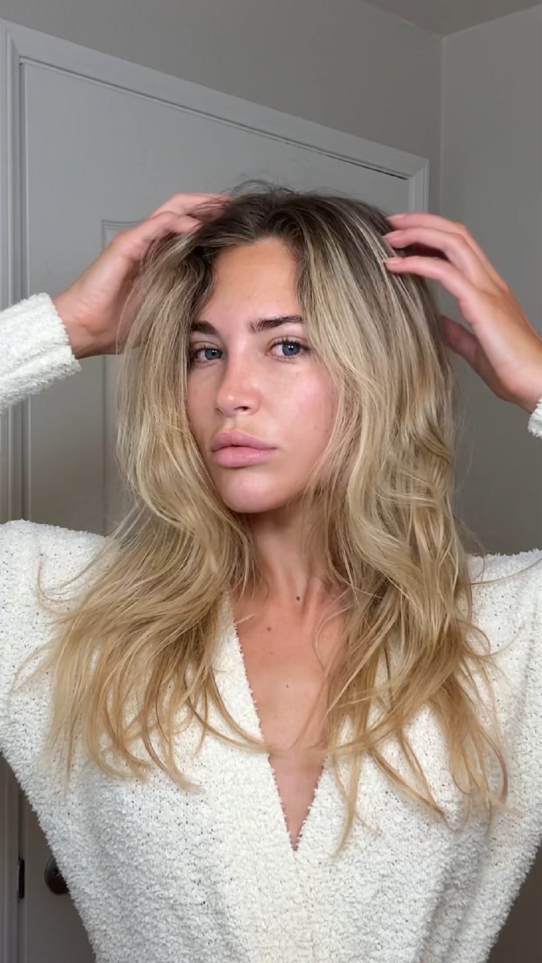 A woman with messy, frizzy hair shown from the back. Her brown hair looks dry, tangled, and lacks shine and smoothness, conveying a damaged or in-need-of-care appearance. She wears a light-colored top, with a simple background that emphasizes the texture and condition of her hair.